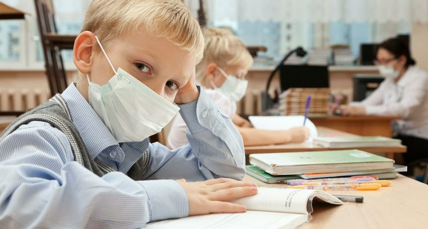 School children in medical face mask are learning in the half empty classroom during epidemic of flu.